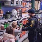 Lombard police officer helping two children pick out sports equipment in a store aisle