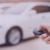 Hand holding a car key fob with a parked car in the background