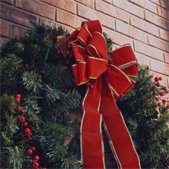 Holiday wreath with red berries and a large red bow hanging on a brick wall