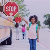 young school girl standing next to yellow school bus pointing at the extended stop sign