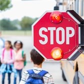 photo of stop sign extended from yellow school bus with young students in background