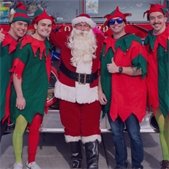 Santa Claus standing with four people dressed as elves in front of a fire truck