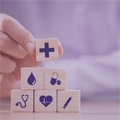 Person stacking wooden blocks with medical symbols including cross, heart, stethoscope, syringe, pill, and water drop