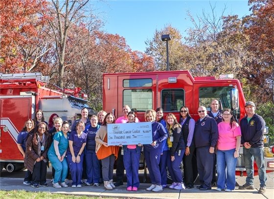 Firefighters and hospital staff standing in front of a fire truck holding a large donation check for the Bhorade Cancer Center