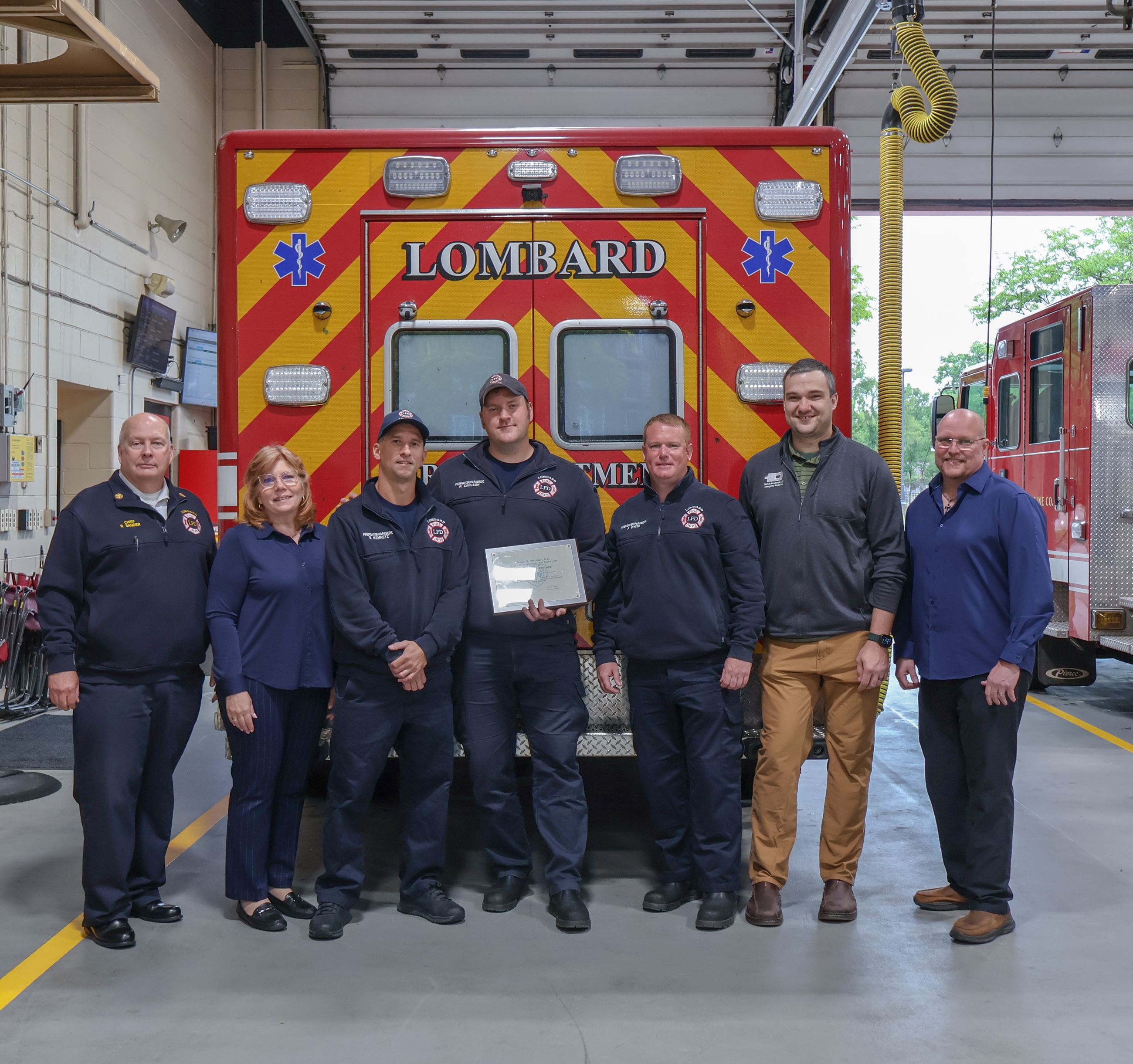group photo of firefighters and hospital officials holding award and back of ambulance in background